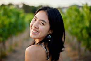headshot-of-happy-asian-woman-walking-through-vineyard (About Us)